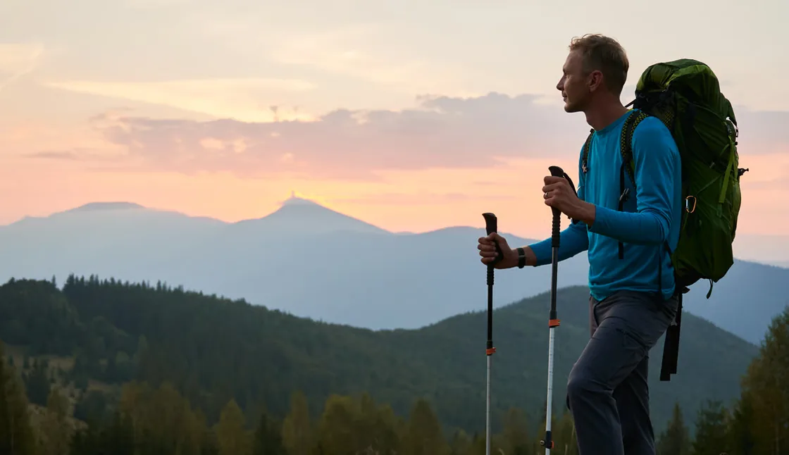 Randonneur équipé au sommet d'une colline, face à des crêtes bleutées au coucher du soleil