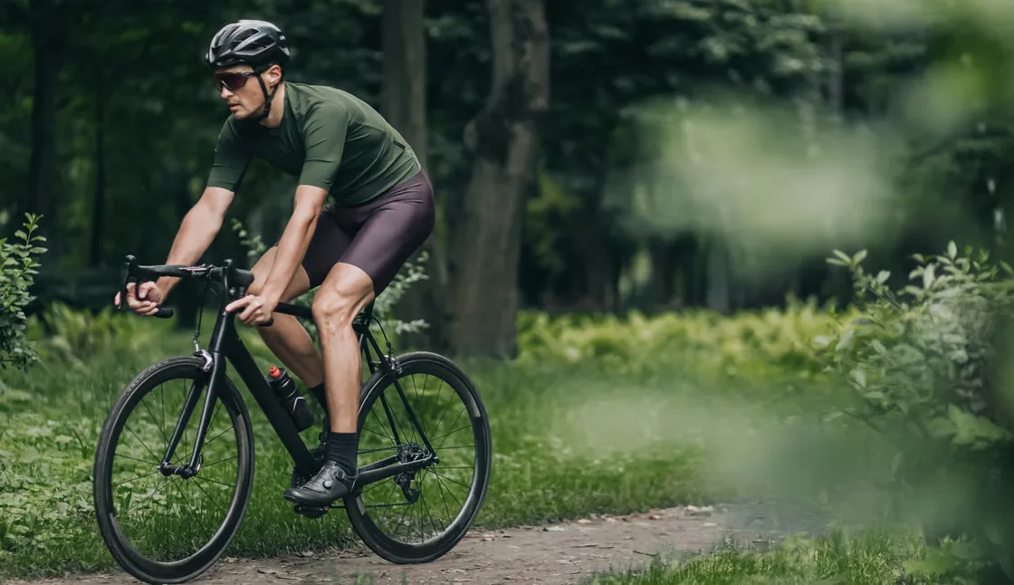 Cycliste en maillot vert olive lancé sur un chemin forestier
