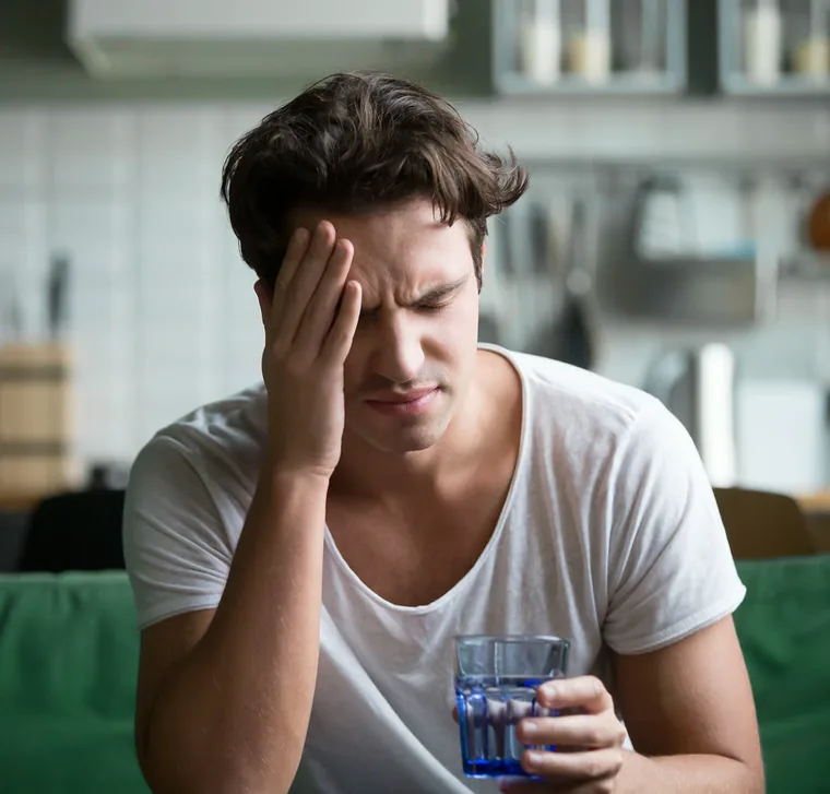 Homme assis dans sa cuisine, la main sur la tempe, marqué par la fatigue